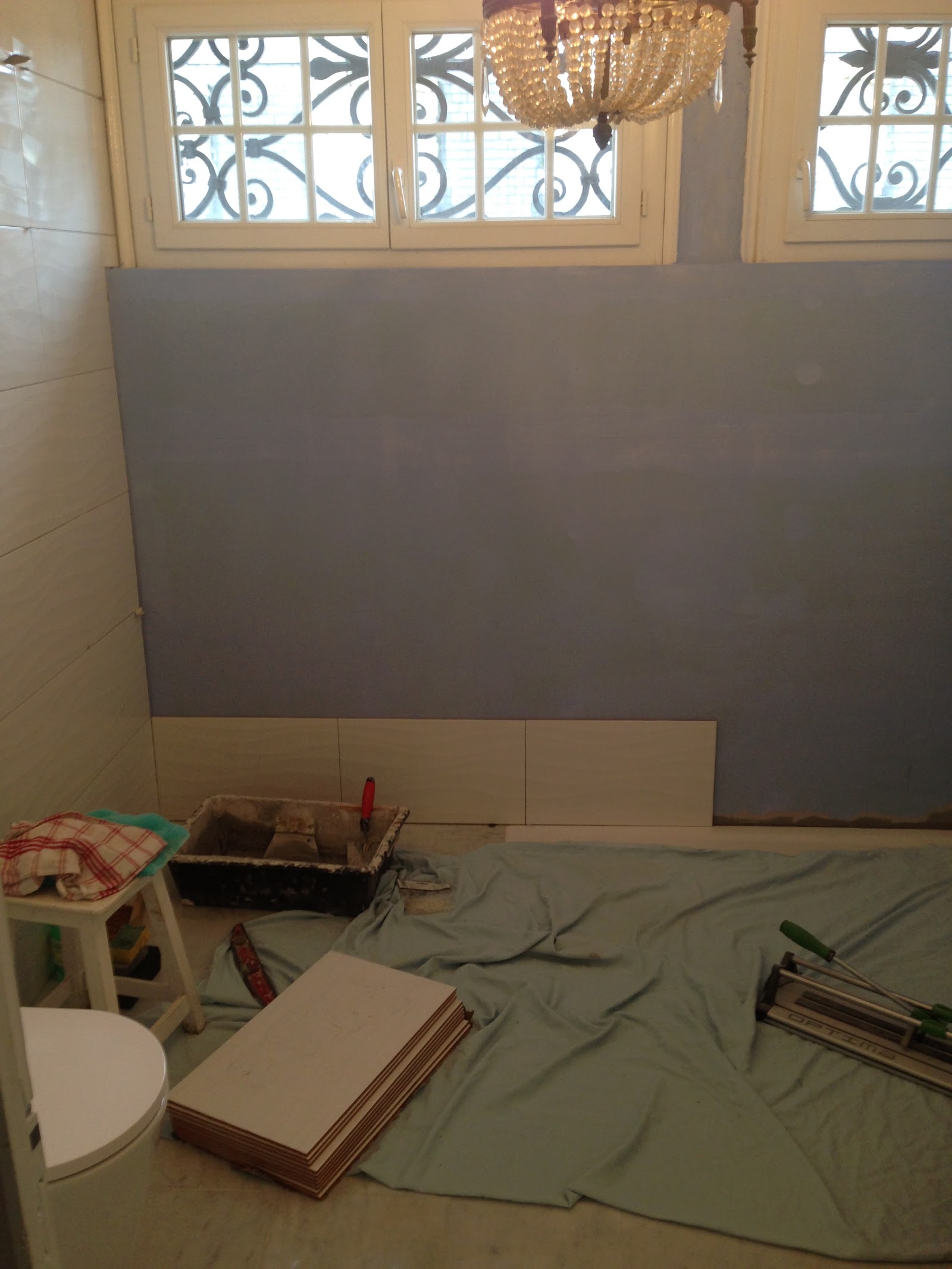 Pose de carrelage mural grand format en cours.